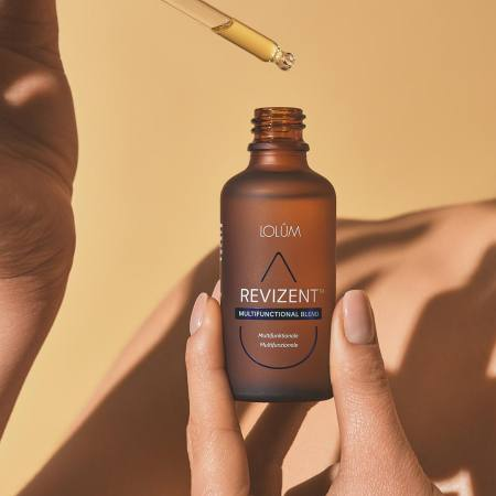 REVIZENT™ Lolûm – flacon compte-gouttes tenu en main, huile multifonctionnelle